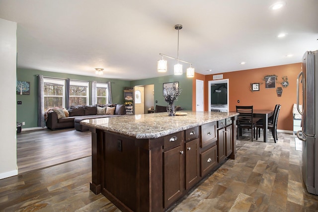 kitchen featuring a center island, freestanding refrigerator, dark brown cabinetry, pendant lighting, and light stone counters