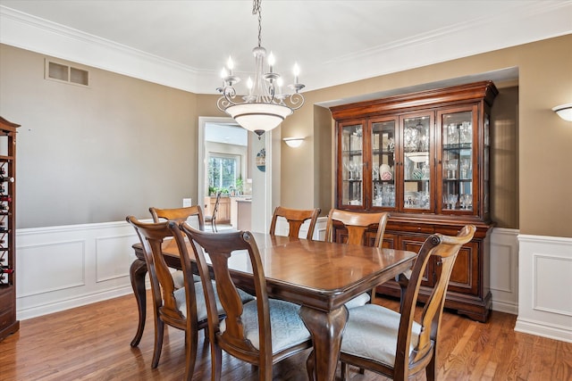 8504 Riverwalk Dr, Fenton, MI 48430 - dining room with a decorative wall, a chandelier, light wood-style flooring, wainscoting, and crown molding