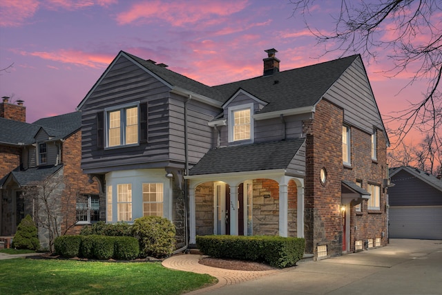 traditional-style house with a chimney, stone siding, roof with shingles, and a yard