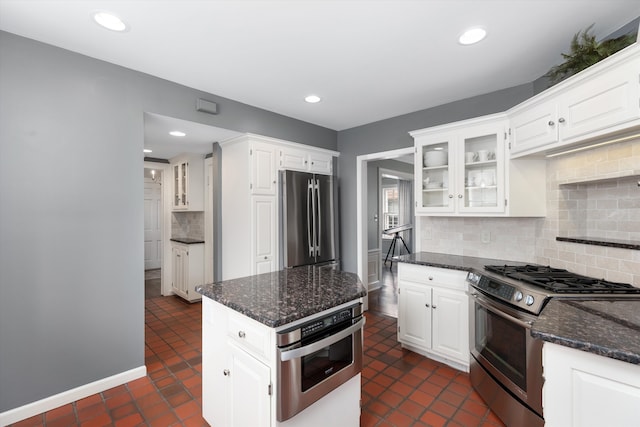 kitchen with appliances with stainless steel finishes, dark stone countertops, decorative backsplash, glass insert cabinets, and white cabinetry