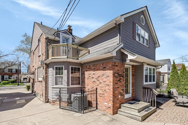 rear view of house with a balcony, brick siding, and fence