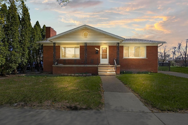 bungalow featuring a porch, a front lawn, brick siding, and a chimney