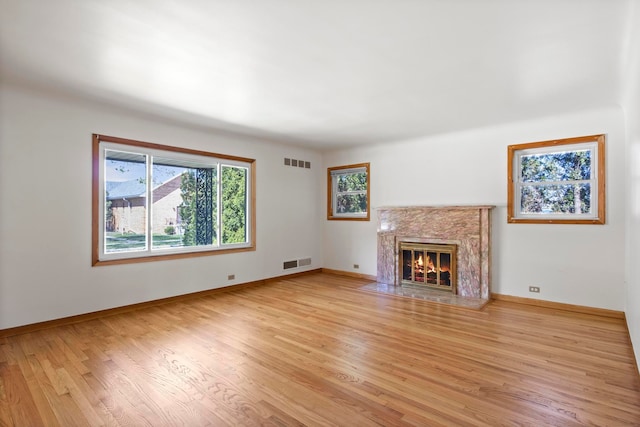 unfurnished living room featuring a premium fireplace, wood finished floors, visible vents, and baseboards