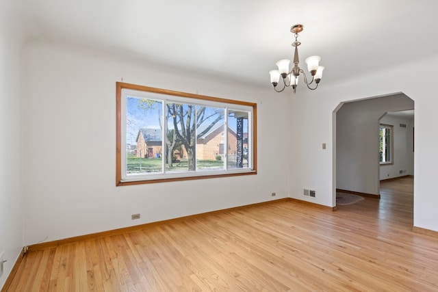unfurnished room featuring arched walkways, an inviting chandelier, light wood-type flooring, and plenty of natural light