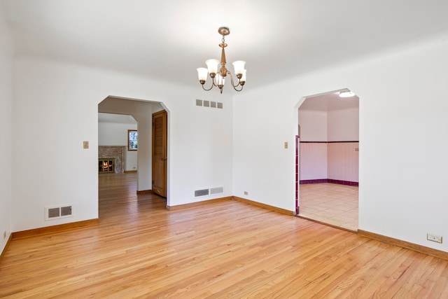 empty room with light wood-type flooring, visible vents, and an inviting chandelier