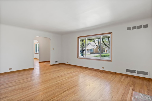unfurnished room with arched walkways, visible vents, and light wood-type flooring