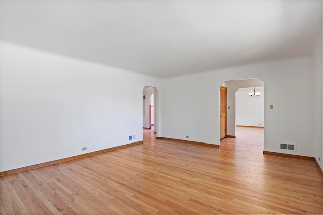 unfurnished room featuring light wood finished floors, an inviting chandelier, visible vents, arched walkways, and baseboards