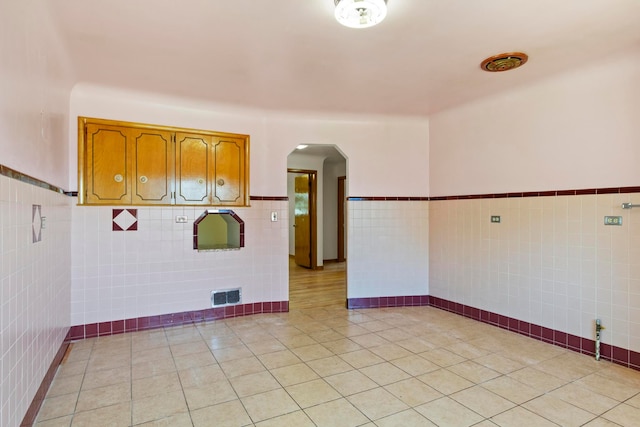 spare room with a wainscoted wall, visible vents, light tile patterned flooring, arched walkways, and tile walls