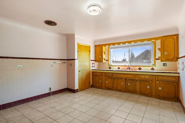 kitchen with brown cabinetry, light tile patterned floors, a sink, and tile walls
