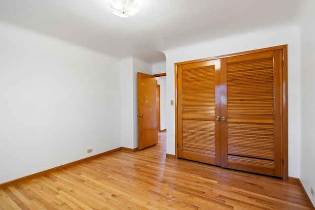 unfurnished bedroom featuring light wood finished floors, baseboards, and a closet