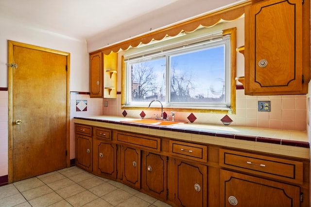 kitchen with backsplash, a sink, brown cabinets, and light tile patterned floors
