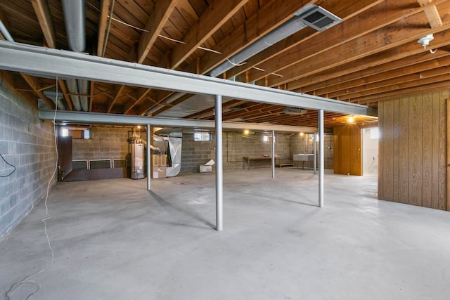 unfinished below grade area with visible vents, concrete block wall, heating unit, and water heater