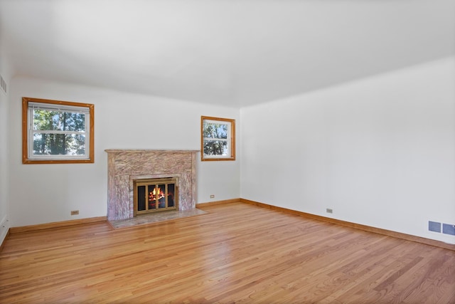 unfurnished living room featuring a high end fireplace, baseboards, light wood-style floors, and visible vents