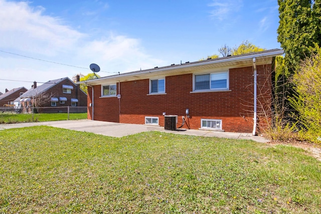 rear view of property featuring central AC unit, fence, brick siding, a patio area, and a yard
