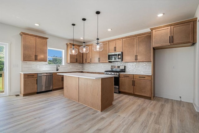 kitchen featuring decorative backsplash, light countertops, pendant lighting, stainless steel appliances, and light wood finished floors