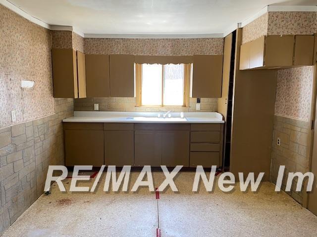5225 N Vassar Rd, Akron, MI 48701 - kitchen featuring wallpapered walls, light countertops, a sink, and ornamental molding