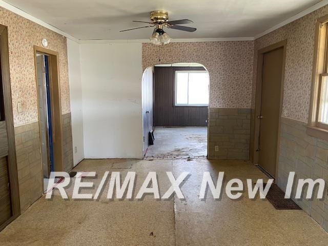 5225 N Vassar Rd, Akron, MI 48701 - unfurnished room with a ceiling fan, crown molding, wallpapered walls, wainscoting, and arched walkways