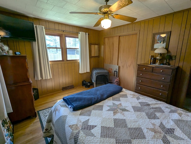 bedroom with light wood-style floors, a closet, a ceiling fan, and wooden walls