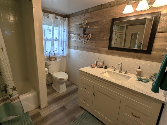 bathroom featuring toilet, shower / bath combo with shower curtain, wood walls, wood finished floors, and vanity