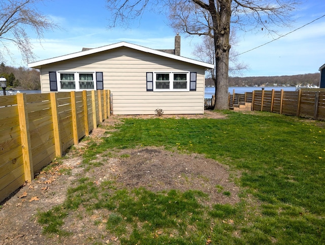 rear view of house with a yard, fence private yard, a chimney, and a water view