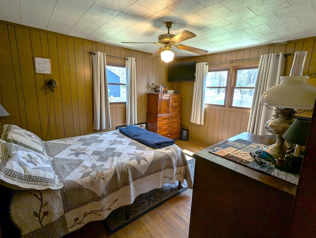bedroom featuring wood walls, hardwood / wood-style flooring, and multiple windows