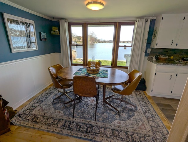 dining room with a healthy amount of sunlight, a wainscoted wall, light wood-type flooring, and a water view