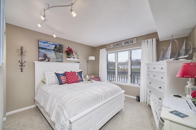 bedroom with light carpet, track lighting, baseboards, and a water view