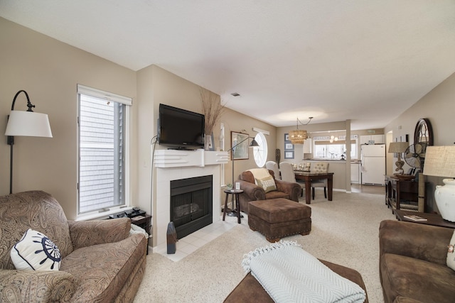 living room featuring light carpet, a tile fireplace, baseboards, and a notable chandelier