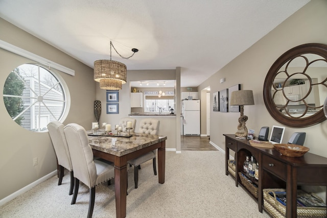 dining space featuring light colored carpet, baseboards, and a chandelier