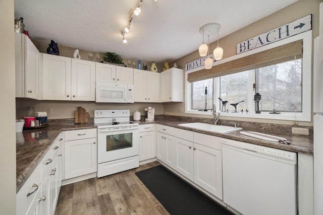 kitchen featuring white cabinets, dark countertops, white appliances, and a sink