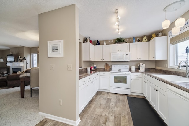 kitchen with white cabinets, a sink, open floor plan, baseboards, and white appliances