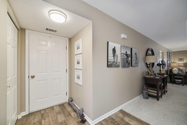 interior space featuring baseboards, visible vents, a textured ceiling, and light wood-style floors