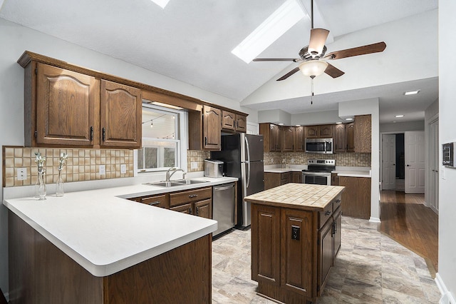 kitchen with stainless steel appliances, a peninsula, a sink, backsplash, and a ceiling fan
