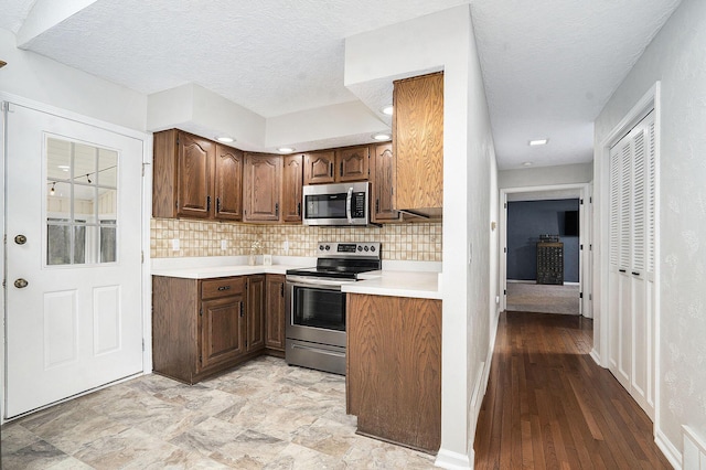 kitchen featuring stainless steel appliances, light countertops, backsplash, baseboards, and a textured ceiling