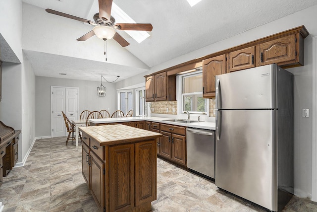 kitchen with stainless steel appliances, a sink, vaulted ceiling, a ceiling fan, and tile countertops