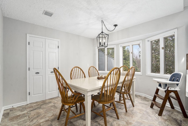 dining room with a textured ceiling, baseboards, stone finish floor, and a notable chandelier