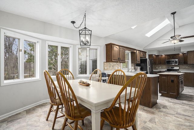 dining space featuring ceiling fan with notable chandelier, baseboards, lofted ceiling with skylight, and a textured ceiling