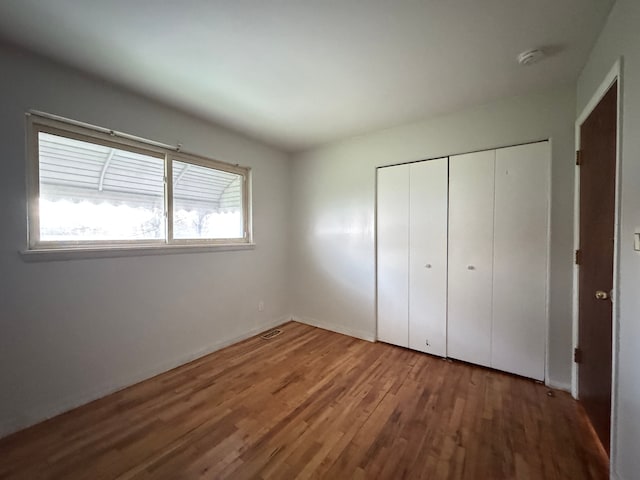 unfurnished bedroom with a closet, baseboards, wood finished floors, and visible vents