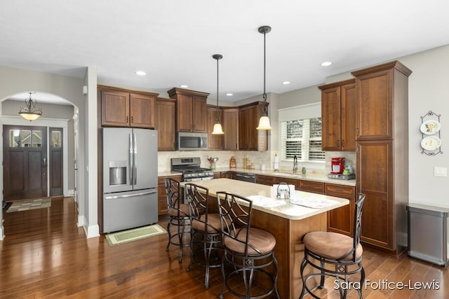 6501 Andres Xing Unit 14, Grandville, MI 49418 - kitchen featuring stainless steel appliances, arched walkways, dark wood finished floors, decorative backsplash, and a breakfast bar