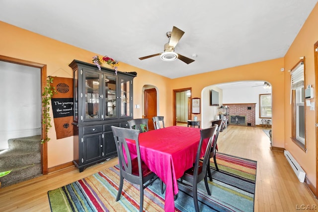 dining space featuring ceiling fan, arched walkways, light wood-style floors, and a baseboard radiator