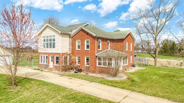 view of front of house with brick siding, driveway, a front lawn, and fence