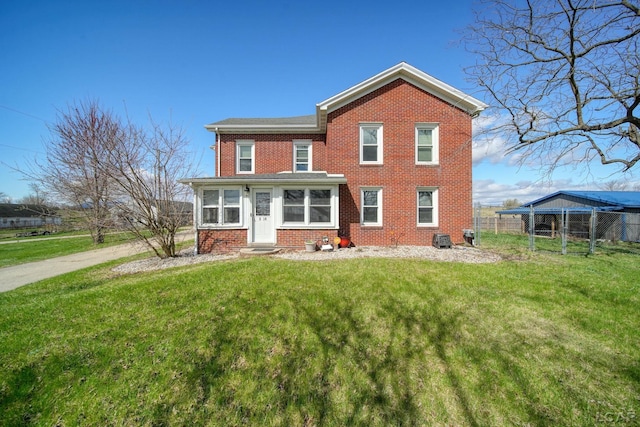 rear view of house with fence, entry steps, brick siding, and a yard
