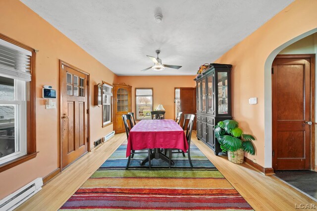 dining space featuring a ceiling fan, arched walkways, light wood-style floors, baseboards, and a baseboard radiator