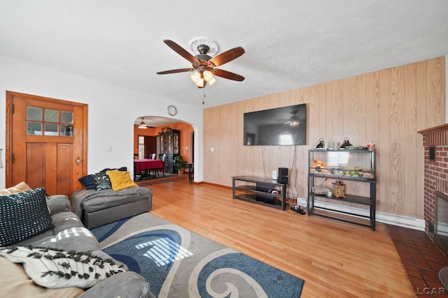 living area with wood finished floors, wooden walls, ceiling fan, arched walkways, and a fireplace