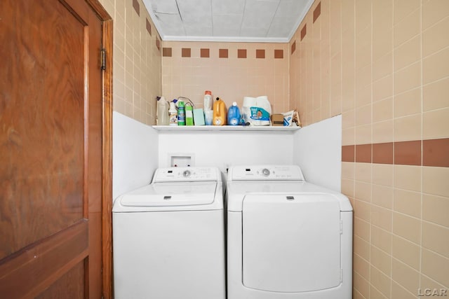 clothes washing area featuring washing machine and dryer, tile walls, and laundry area