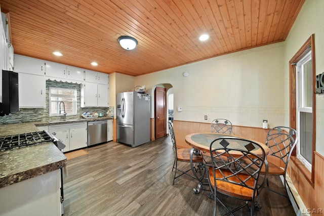 kitchen with arched walkways, a baseboard radiator, wooden ceiling, and stainless steel appliances