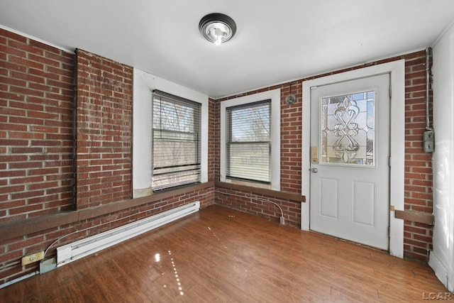 foyer entrance featuring baseboard heating, brick wall, and wood finished floors