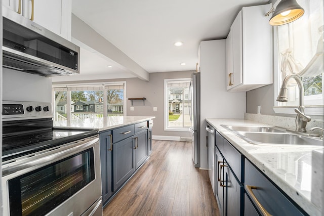 kitchen with appliances with stainless steel finishes, a sink, light wood-style floors, recessed lighting, and light stone counters