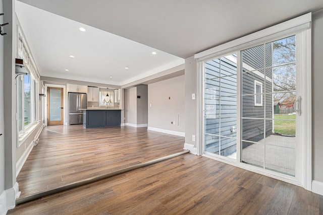 unfurnished living room with wood finished floors, baseboards, recessed lighting, and a sink