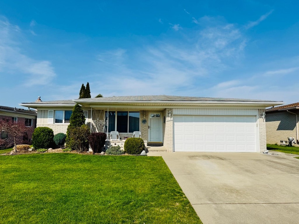 single story home with concrete driveway, a front lawn, brick siding, and a porch